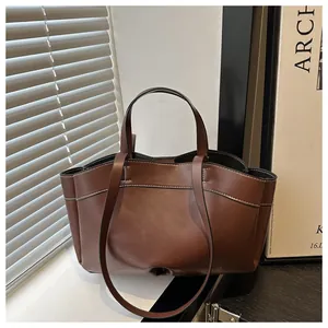 Detail of brown leather tote bag showing white contrast stitching and wavy edge design