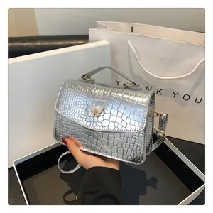 Detail of silver crocodile-embossed leather bag with decorative butterfly buckle and handle