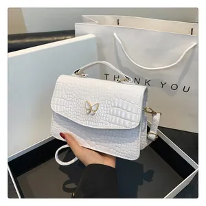 Close-up of white crocodile pattern leather bag with golden butterfly buckle detail