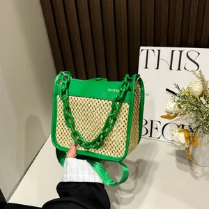 Detail of woven straw handbag with green leather trim and chunky acrylic chain handle