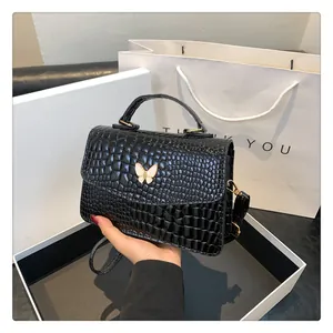 Detail of black faux crocodile skin handbag with a golden butterfly metal clasp