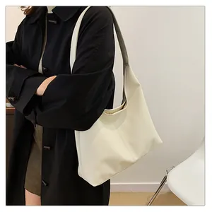 Minimalist creamy white tote bag in soft faux leather shown on a model with black coat
