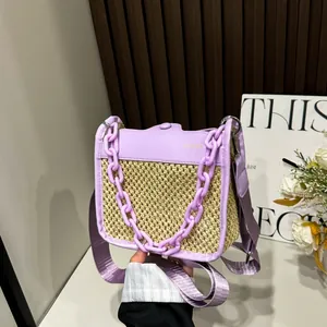 Close-up of hand-held straw crossbody bag with purple leather flap and chain detail