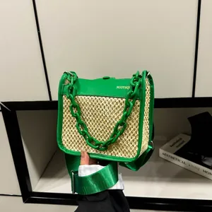 Detail of woven straw crossbody bag with green trim, acrylic chain and gold logo