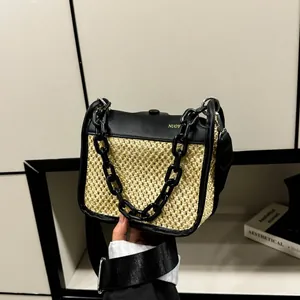 Detail of woven straw handbag with black leather trim, gold logo and chunky chain strap
