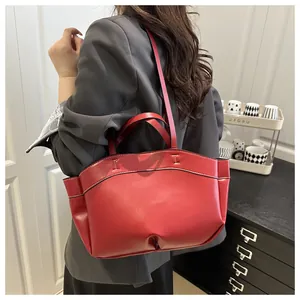 Macro detail of red leather tote bag showing white contrast stitching and pleated sides