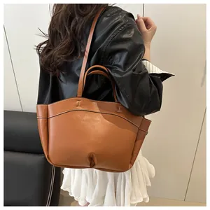 Close-up of brown leather tote bag featuring wavy opening and H-shaped metal buckle