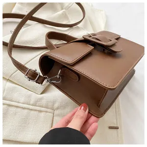 Macro detail of brown leather crossbody bag featuring a large decorative square buckle