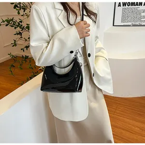 Sac croissant noir brillant avec chaîne argentée présenté sur un fond blanc minimaliste
