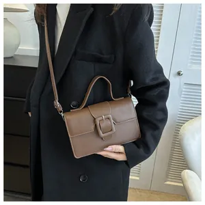Detail of a brown leather crossbody bag with a large square buckle on a long black coat