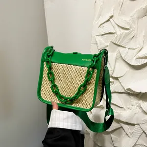 Green woven straw crossbody bag with contrast leather trim and decorative chain strap