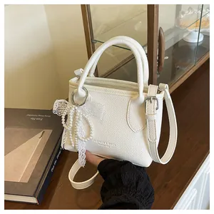 Detail of white lychee leather bucket bag with pearl lace bow and adjustable strap
