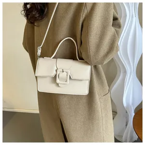 Detail of a beige minimalist crossbody bag styled on a brown coat for fall/winter fashion