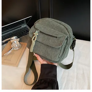 Detail of army green corduroy crossbody bag featuring a zipped front pocket and woven pendant