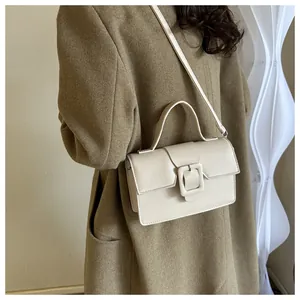 Detailed view of cream leather handbag with large square buckle and top handle grip