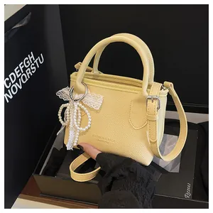 Detail of light yellow lychee grain leather handbag with pearl and lace bow charm