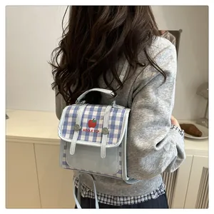 Detail of blue plaid mini backpack featuring red apple embroidery and leather flap cover