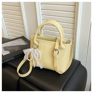 Detail of yellow pebbled leather bag with pearl bow charm and logo text on the front
