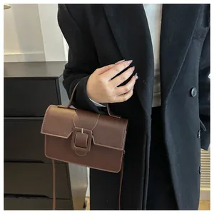 Detail view of retro brown leather handbag with minimalist square buckle and handle