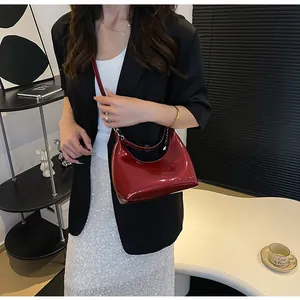 Détail du sac croissant en cuir verni bordeaux avec chaîne en métal et finition lisse