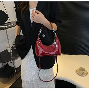 Détail du sac croissant en cuir verni rouge foncé avec breloque et logo embossé