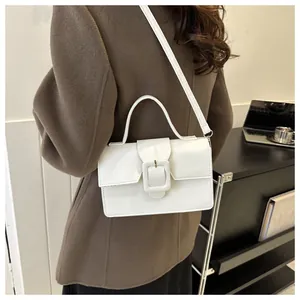 White minimalist crossbody bag with top handle and decorative buckle in a lifestyle setting