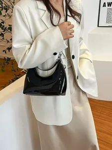 Sac croissant noir brillant avec chaîne argentée porté par un mannequin en blazer