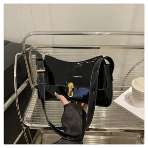 Detail of glossy black patent leather shoulder bag with elegant gold metal cylinder lock