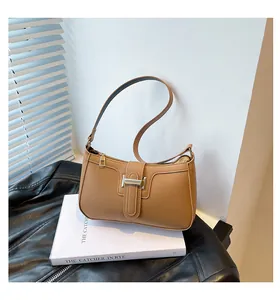 Detailed close-up of brown faux leather underarm bag with metal buckle on a leather jacket