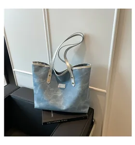 Close-up of blue denim tote bag featuring silver FASHION label and metallic handles
