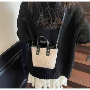 Detail of a beige bucket bag with black trim and gold-tone studs shown on a model