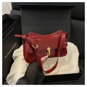 Macro view of burgundy patent leather shoulder bag with gold clasp in a black gift box