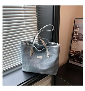 Detail of grey tote bag with silver edging and stitched fashion label on window sill
