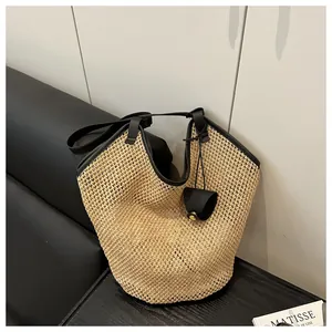 Detail of handwoven straw tote bag with black leather piping and mini charm on wood table