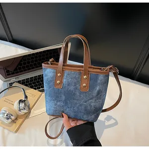 Detail of blue denim and brown leather bucket bag with gold rivets on a minimalist desk