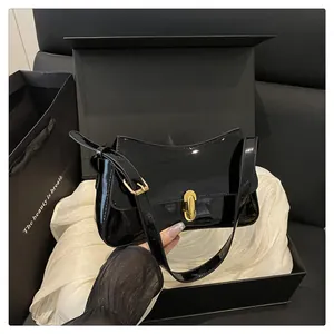 Detail of glossy black patent leather shoulder bag with elegant gold metal clasp and buckle