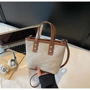 Detail of canvas bucket bag with leather trim alongside a laptop and headphones