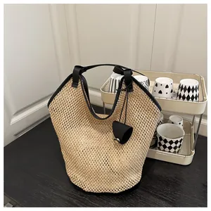 Detailed close-up of straw beach tote bag with black leather handles and matching small pouch