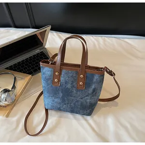 Detail of blue denim bucket bag with brown leather handles and golden rivets on bed