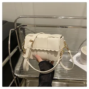 Detail of white woven flap bag with scalloped edges and adjustable shoulder strap