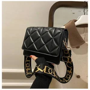 Close-up of black quilted small square bag with decorative wide fabric shoulder strap