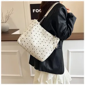 Detail of cream tote bag with black bow patterns, metal chain and pearl pendant accessory