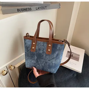 Detail of a denim tote bag featuring brown leather trim and golden rivets for a vintage look