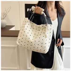Close-up of white tote bag with black bow embroidery and pearl bow pendant detail