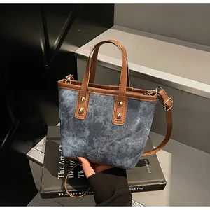 Detail of blue denim handbag with brown leather handles and golden metal rivets decoration