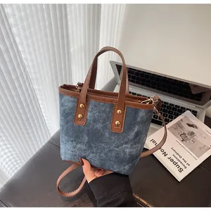 Detail of denim bucket bag with brown leather straps and gold metal rivet accents