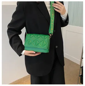 Green crossbody bag with triangular quilting and wide strap on a black blazer