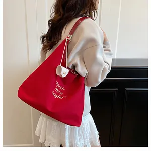 Detail of red large capacity canvas tote bag with letter embroidery and charm on model