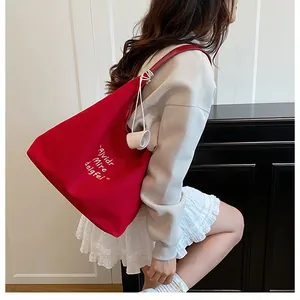 Detail view of large red canvas tote bag featuring white cursive embroidery and charm