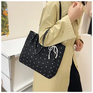 Detail of black pleated tote bag with bow pattern and pearl butterfly pendant accessory